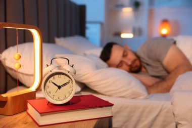 Evde uyuyan genç adam, çalar saate ve kitaba odaklan.