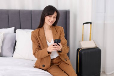 Otel odasında akıllı telefonu olan bir iş kadını.
