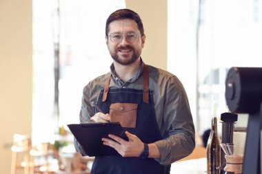 Kahvesinde panoyla çalışan gülümseyen bir işletme sahibi.