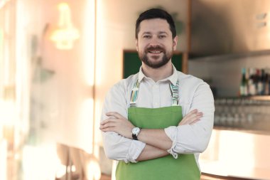 Kafesinde kollarını kavuşturmuş gülümseyen bir işletme sahibinin portresi. Metin için boşluk