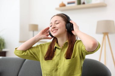 Kulaklıklı genç kız evdeki kanepede müzik dinliyor.