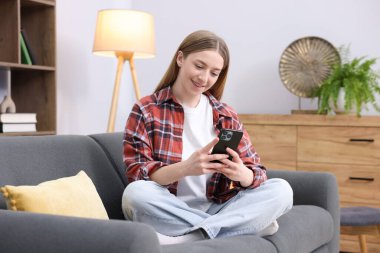 Evdeki kanepede dizüstü bilgisayarlı gülümseyen genç kız.