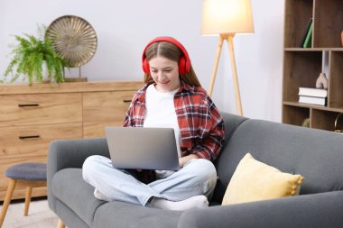 Evdeki kanepede dizüstü bilgisayarlı gülümseyen genç kız.
