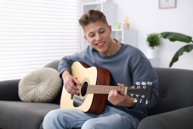 Mutlu adam içeride kanepede gitar çalıyor.