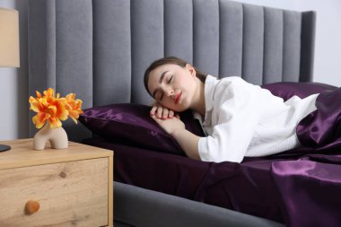 Mor ipek çarşaflarla yatakta uyuyan bir kadın.