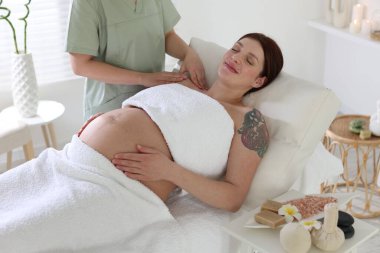 Hamile kadın spa salonunda rahatlatıcı bir masaj yaptırıyor.