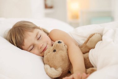 Yatma vakti. Tatlı küçük kız yatakta oyuncak ayıyla uyuyor.