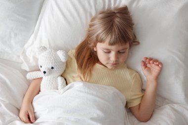 Yatma vakti. Oyuncak ayıyla yatakta uyuyan tatlı küçük kız.