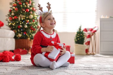Evde hediye kutularıyla Noel kostümü giymiş küçük kız.
