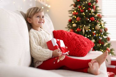 Noel hediyesi kutulu küçük kız evdeki kanepede oturuyor.