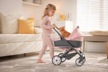 Evinde oyuncak bebek arabasında kızıl kedisi olan sevimli küçük bir kız.