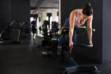 Spor salonundaki T-Bar sıra makinesinde ağırlık plakalı atletik kadın antrenmanı. Metin için boşluk
