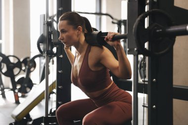 Spor salonunda Smith makinesinde halterli kadın antrenmanı