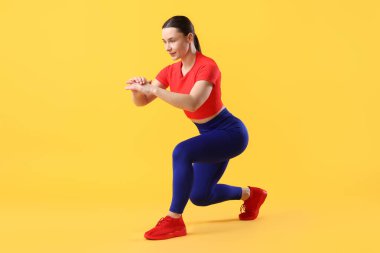 Spor kıyafetli kadın turuncu arka planda egzersiz yapıyor.