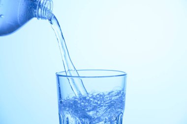 Pouring soda water from bottle into glass on light blue background, closeup. Space for text