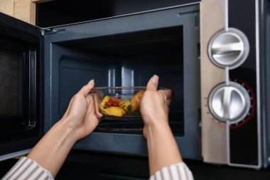 Kadın yemeğiyle birlikte mikrodalgaya konteynır koyuyor. Kapalı mekanda.