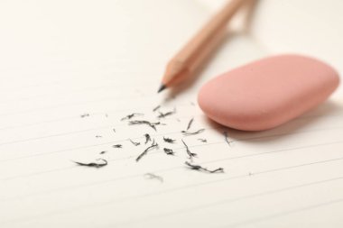 Eraser, pencil and scraps on lined notebook sheet, closeup. Space for text