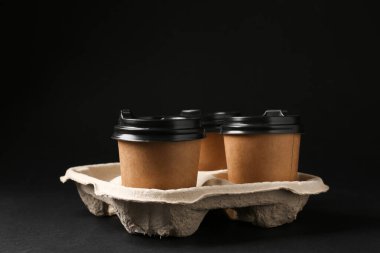 Siyah arka planda karton tutacakta kağıt kahve fincanları.