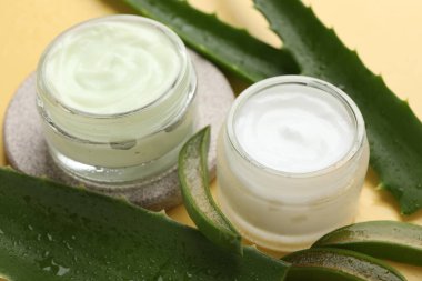 Aloe vera özütüyle nemlendirici krem ve sarı arkaplanda yapraklar, yakın plan.