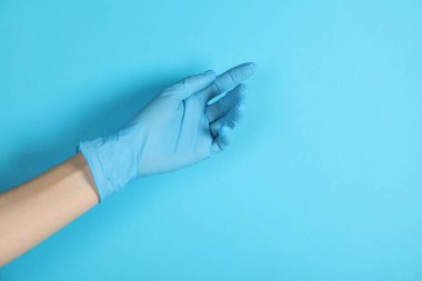 Açık mavi arka planda tıbbi eldiven giyen doktor, yakın plan. Metin için boşluk