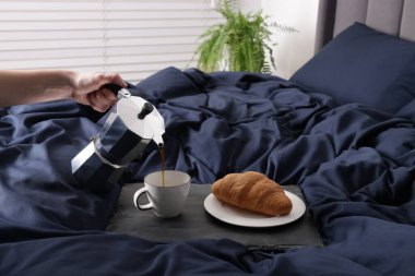 Bir kadın, güzel mavi ipek çarşafları olan bir bardağa kahve dolduruyor.