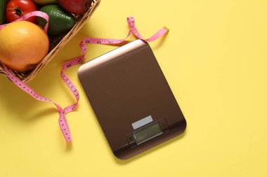 Elektronik mutfak ölçeği, ölçüm bandı ve sarı arka plandaki ürünler, düz alan. Diyet