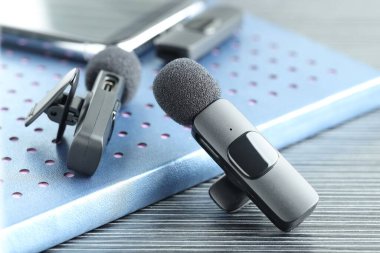 Lavalier mikrofonlar, kablosuz alıcısı olan akıllı telefon ve siyah ahşap masadaki defter, yakın plan.