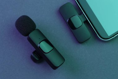 Lavalier mikrofon ve kablosuz alıcısı olan akıllı telefon karanlık masada, neon ışıklarda, düz yatıyordu.