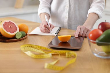 Turuncu ağırlıklı kadın, ahşap masada deftere yazı yazıyor, yakın plan.