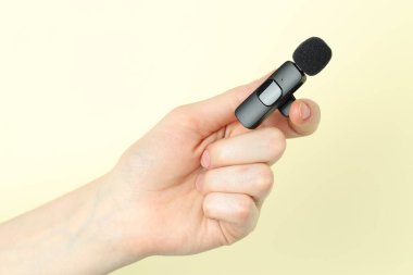 Bej arka planda lavalier mikrofon tutan kadın, yakın plan.