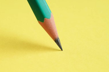 Sarı arka planda keskin bir grafit kalem, yakın plan.