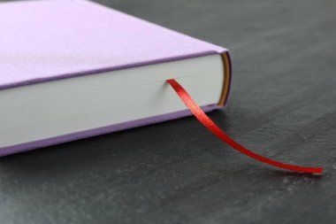 Koyu desenli masa üzerinde kırmızı kurdele yer imi olan kitap, yakın plan.