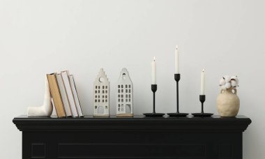 Beyaz duvarın yanındaki şöminede yanan mumlar ve diğer dekorlarla süslü şamdanlar.