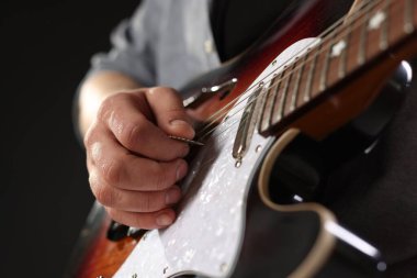 Siyah arkaplanda arabulucuyla gitar çalan adam, yakın plan