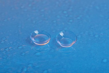 Mavi ayna yüzeyine bir çift kontakt lens ve su damlası, yakın plan.