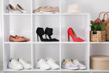 Ayakkabı deposu. Beyaz duvarın yanında farklı ayakkabı ve dekorlarla raf ünitesi.