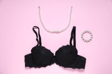 Pembe arka planda siyah dantelli sütyen ve mücevher.