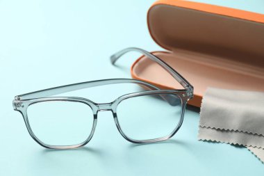 Çanta, şık gözlükler ve açık mavi arka planda temizlik bezi, yakın plan.