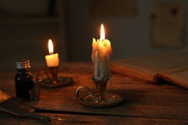 Mumları şamdanlarda yakmak, mürekkep hokkası, dolmakalem ve ahşap masada eski kitaplar.