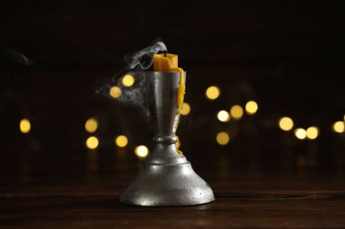 Sönmüş mum, ahşap masada, bulanık ışıklarla kararmış arka planda. Bokeh etkisi
