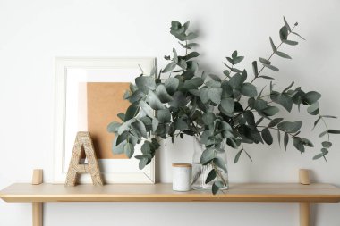 Vazodaki okaliptüs dalları ve beyaz duvarın yanındaki ahşap masa üzerindeki diğer dekorlar.