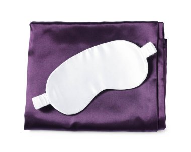 Beyaz arka planda ipek çarşaflar ve uyku maskesi, üst manzara.