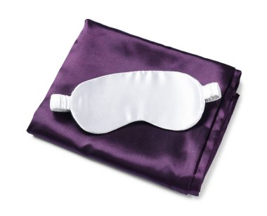 Beyaz arka planda ipek çarşaflar ve uyku maskesi, üst manzara.