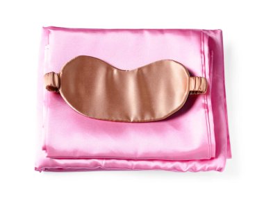 Beyaz arka planda ipek çarşaflar ve uyku maskesi, üst manzara.