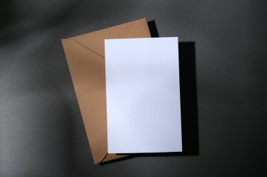Koyu gri arkaplanda boş tebrik kartı ve kağıt zarf, üst görünüm