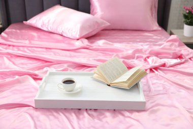 Lüks ipek çarşaflar, kahve tepsisi ve yatakta kitap.