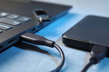 Mavi desenli masadaki dizüstü bilgisayara bağlı USB kablosu olan sabit disk sürücüsü.