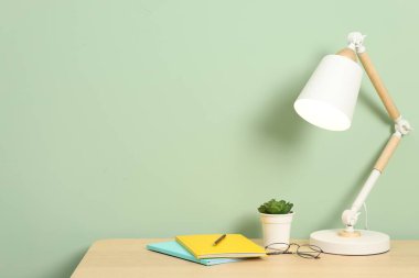 Lambalı, kırtasiyeli ve açık yeşil duvarlı ahşap masadaki bitkilerle süslü bir iş yeri. Metin için boşluk