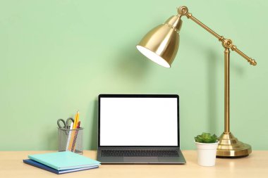 Modern dizüstü bilgisayarlı şık bir iş yeri açık yeşil duvarın yanındaki ahşap masada.