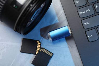 Bilgisayara bağlı flaş bellek, SD hafıza kartları ve gri masadaki kamera lensi, düz konum